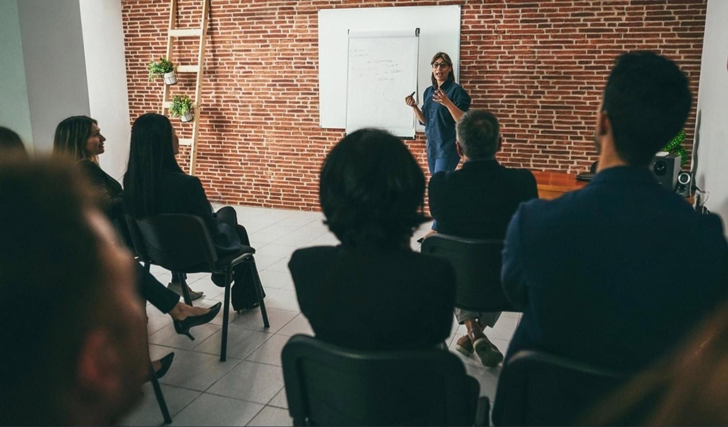 Instructor leading a corporate training workshop with professionals seated in a brick-walled room