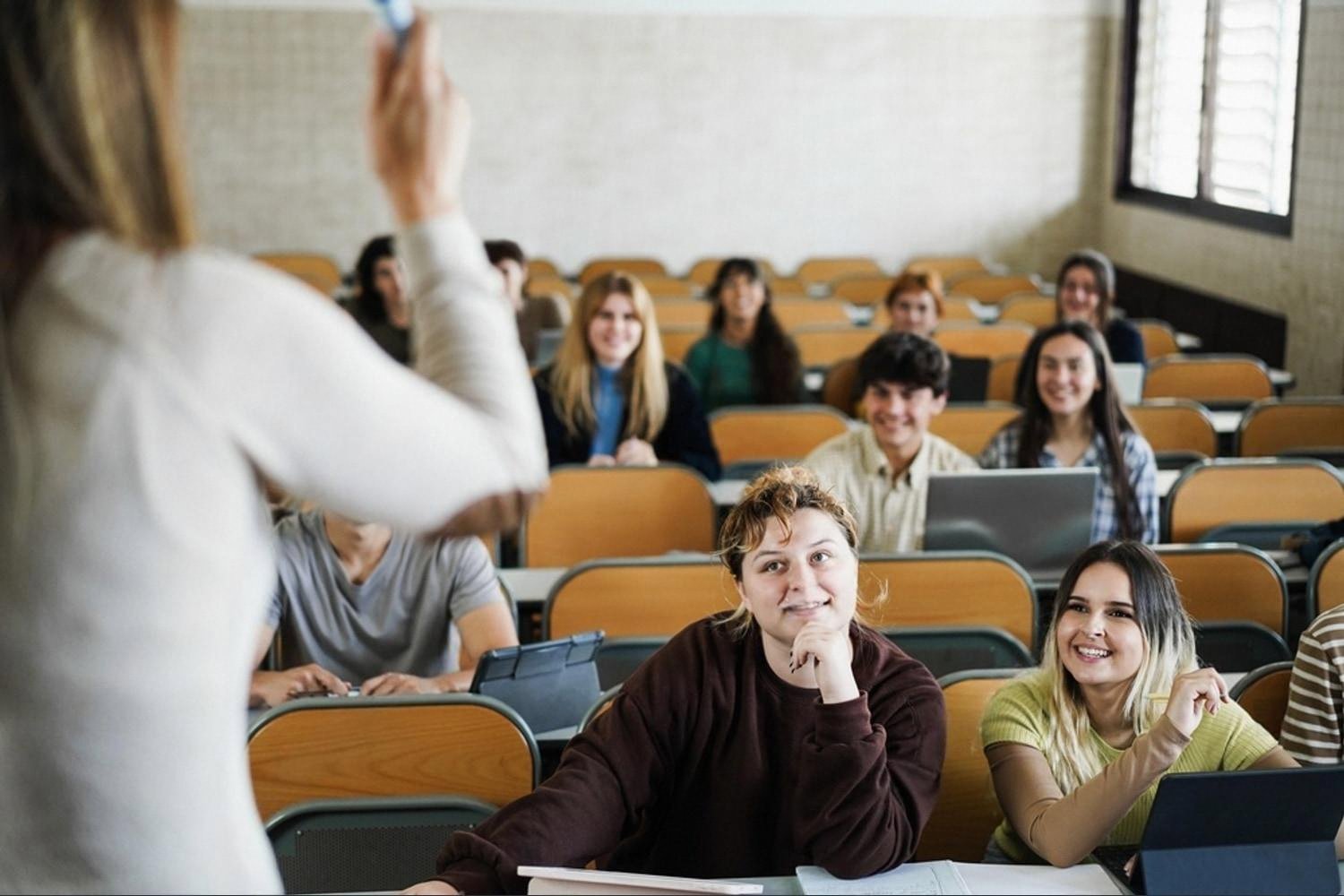 Adult learners in a lecture hall raising hands during a continuing education class